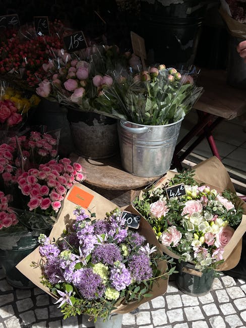 A variety of fresh floral arrangements displayed outdoors at a flower market, featuring pink roses and peonies wrapped in brown paper, purple alliums, and other mixed blossoms in metal buckets and con